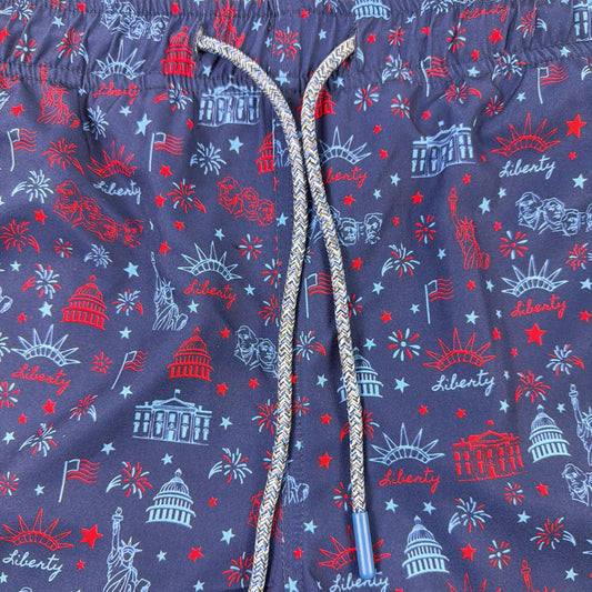 Navy swim shorts with red, white, and blue graphics on a beige background