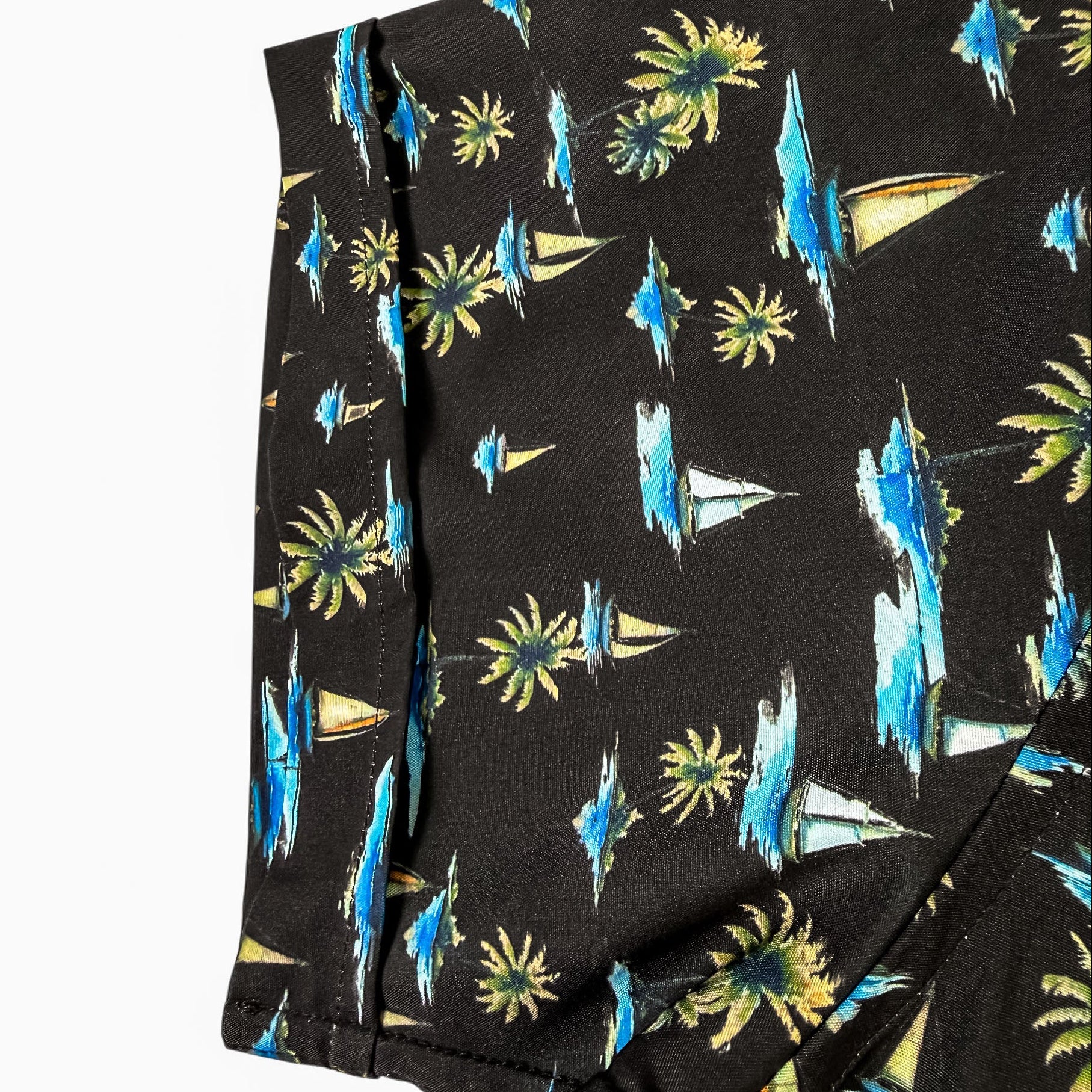Black shorts with tropical pattern featuring palm trees and boats on a white background