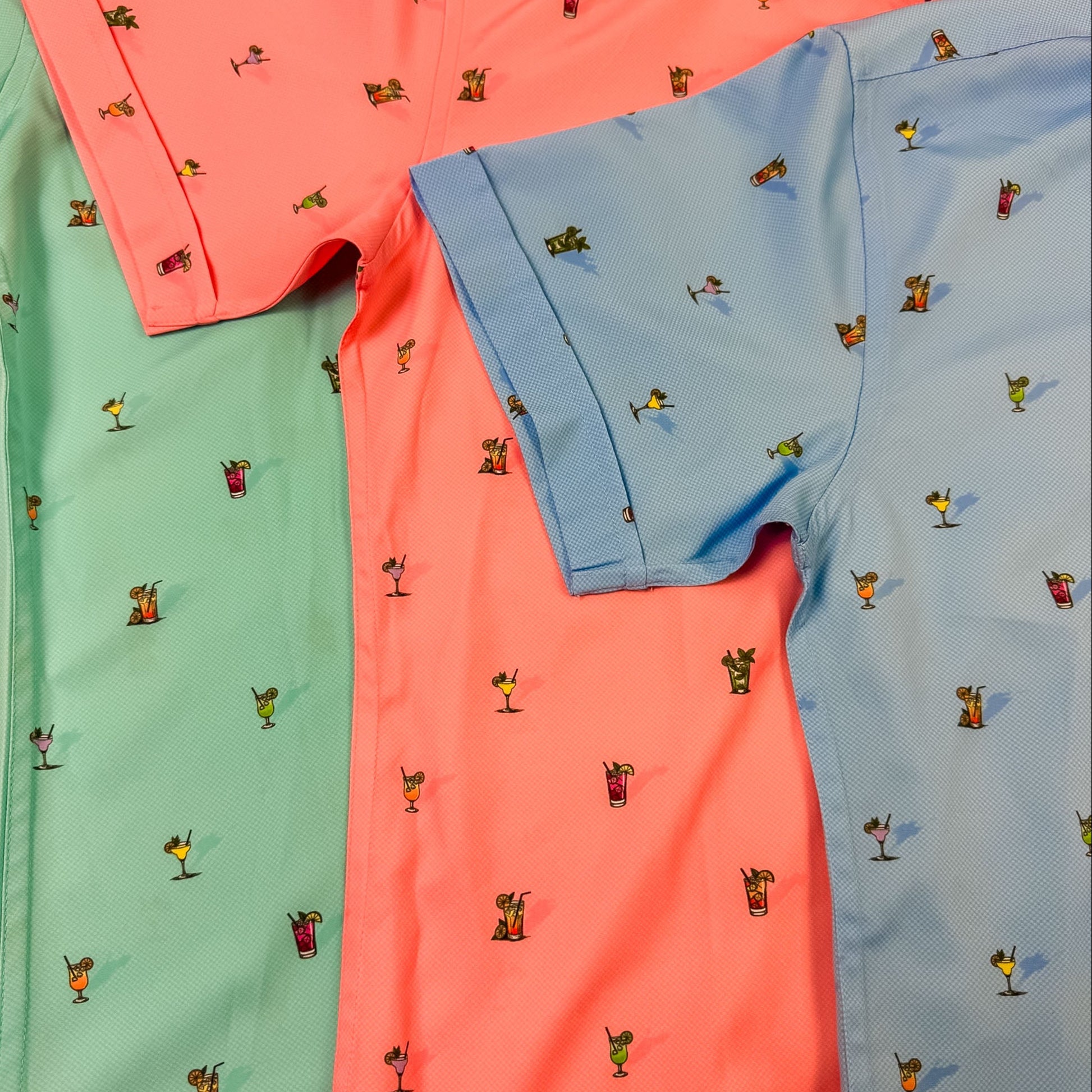Three shirts in green, pink, and blue with small printed patterns on a white background