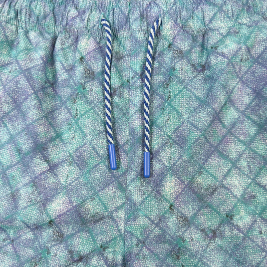 Blue and green patterned shorts with two straws on a beige background